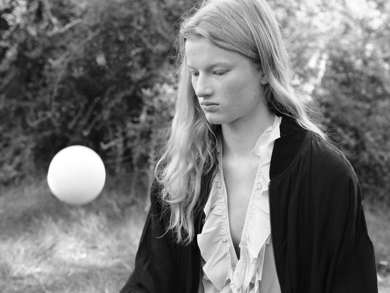 Monochrome portrait of a model with long hair wearing a dark jacket outdoors with a floating white sphere