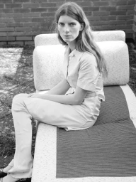Portrait of a woman with long hair seated on an outdoor lounger wearing a collared button-up shirt and trousers
