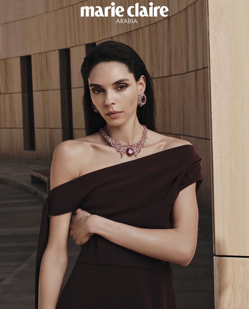 Model wearing a dark one-shoulder dress and gemstone jewellery standing before stone architecture for Marie Claire Arabia