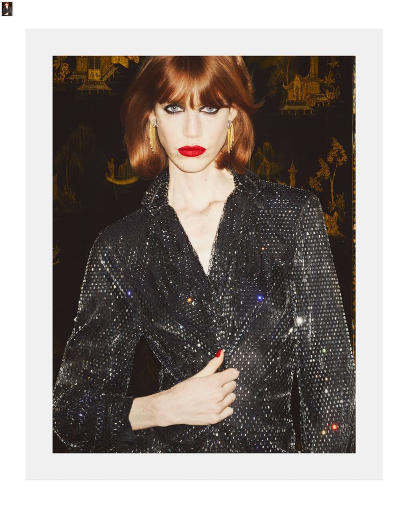 Model Poppy Miles wearing a sparkling black top and red lipstick against a dark patterned background for Harper's Bazaar France.