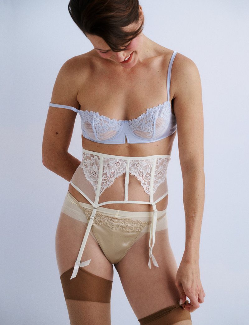 Model in pale blue lace bra and white garter belt against a white backdrop