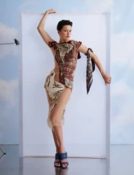 Model posing against a white backdrop with a printed dress and a silk scarf tied to her arm for Vogue Greece