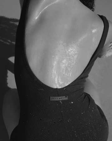 Black and white close-up photo of an adult female wearing a black swimsuit, seen from the back, with water droplets on her skin.