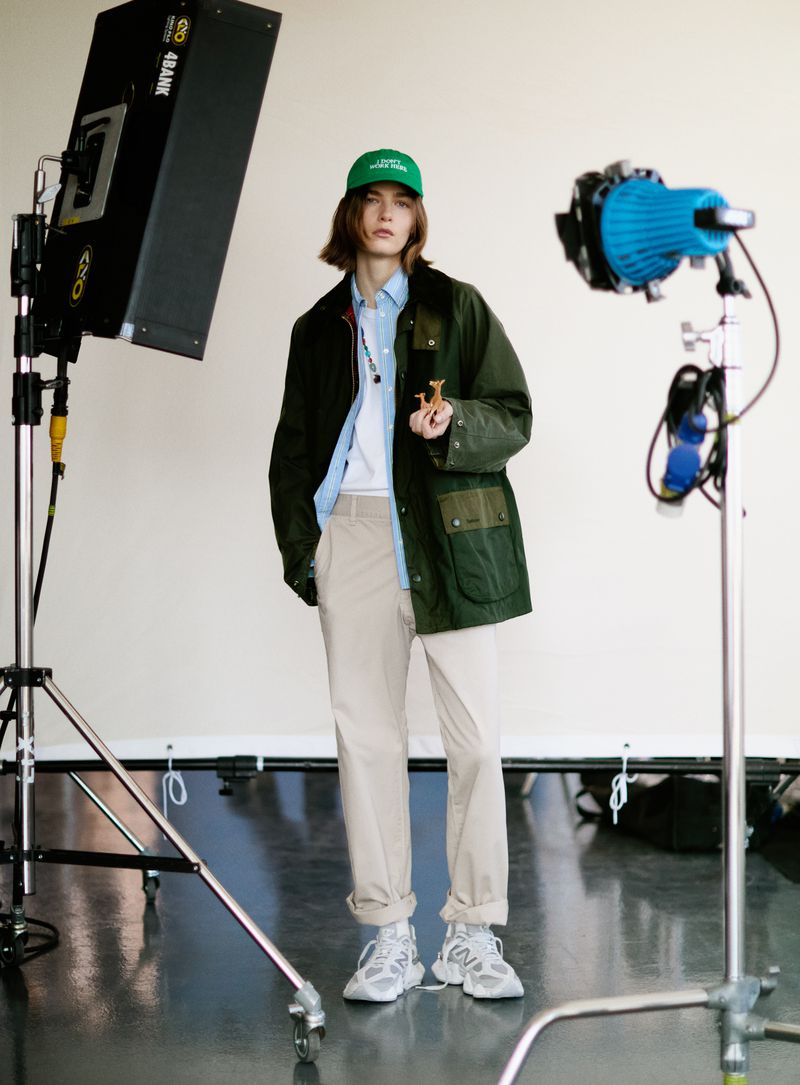 Model in green cap and dark green jacket standing in a studio with lighting equipment
