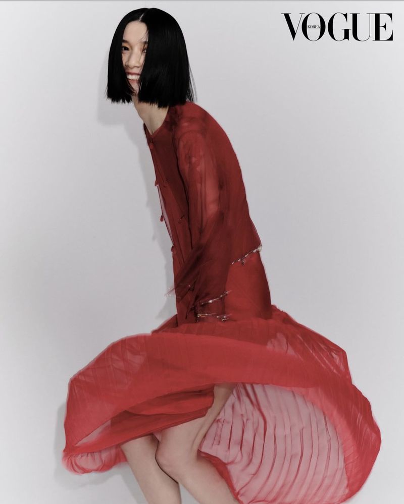 Fashion editorial featuring a smiling Asian woman in a red dress against a white backdrop, Vogue Korea logo visible in the upper right corner.