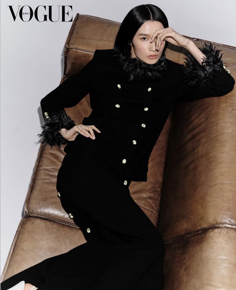 Model Esther Kim wearing a black feather-trimmed jacket on a brown leather sofa for Vogue Korea fashion editorial