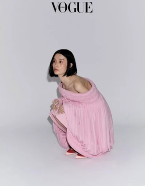 Model Esther Kim in a pink off-the-shoulder dress crouching against a plain light grey studio background for Vogue Korea editorial
