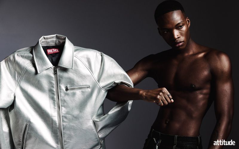 Shirtless man posing next to a metallic silver jacket against a dark grey background for Attitude Magazine