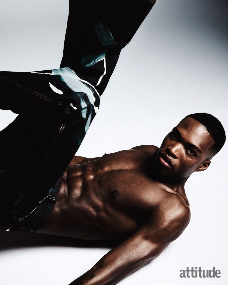 Shirtless black man posing dynamically in dark patterned trousers against a white backdrop for Attitude Magazine