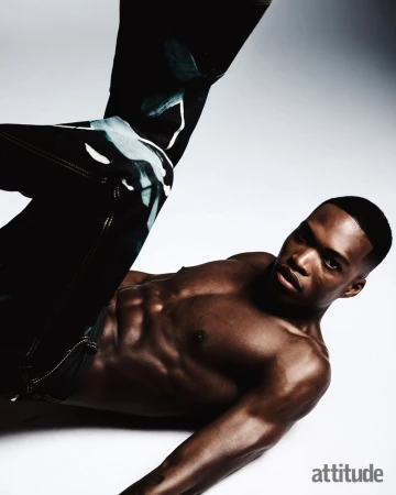 Shirtless black man posing dynamically in dark patterned trousers against a white backdrop for Attitude Magazine