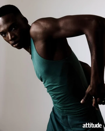 Portrait of a black man wearing a teal tank top posing against a light grey studio background for Attitude Magazine