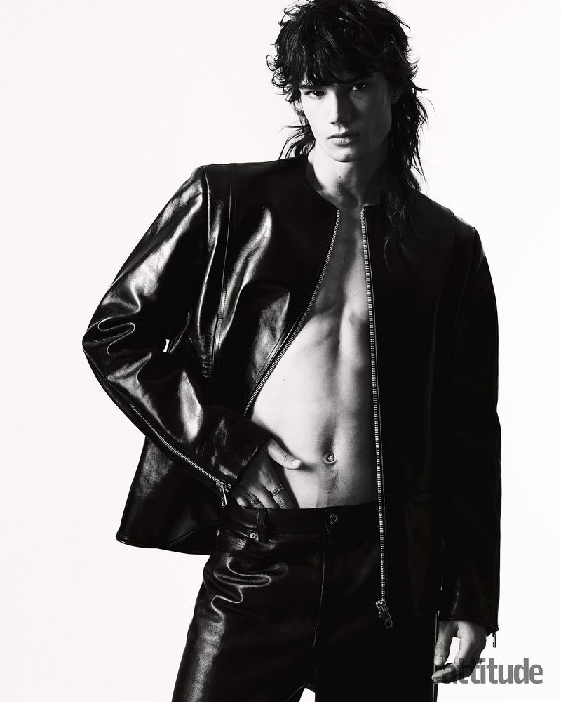 Man with dark shaggy hair wearing an open black leather jacket against a white background for Attitude Magazine