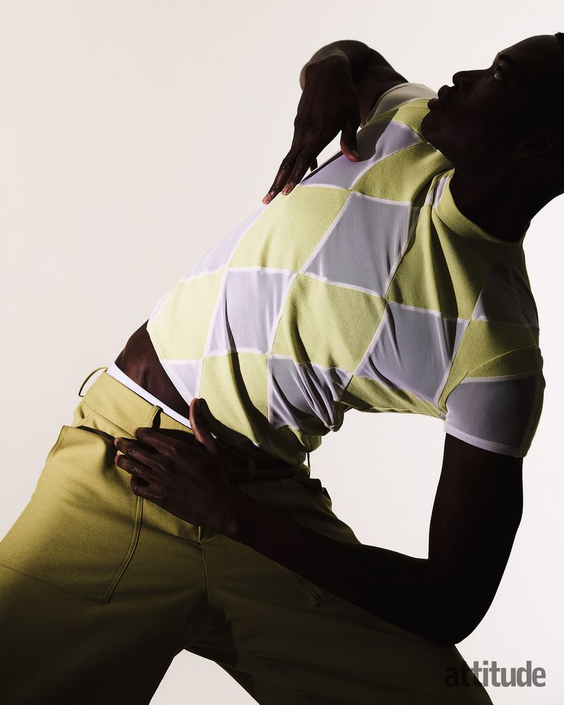 Black man arching back wearing checkered yellow t-shirt and trousers against white background for Attitude Magazine