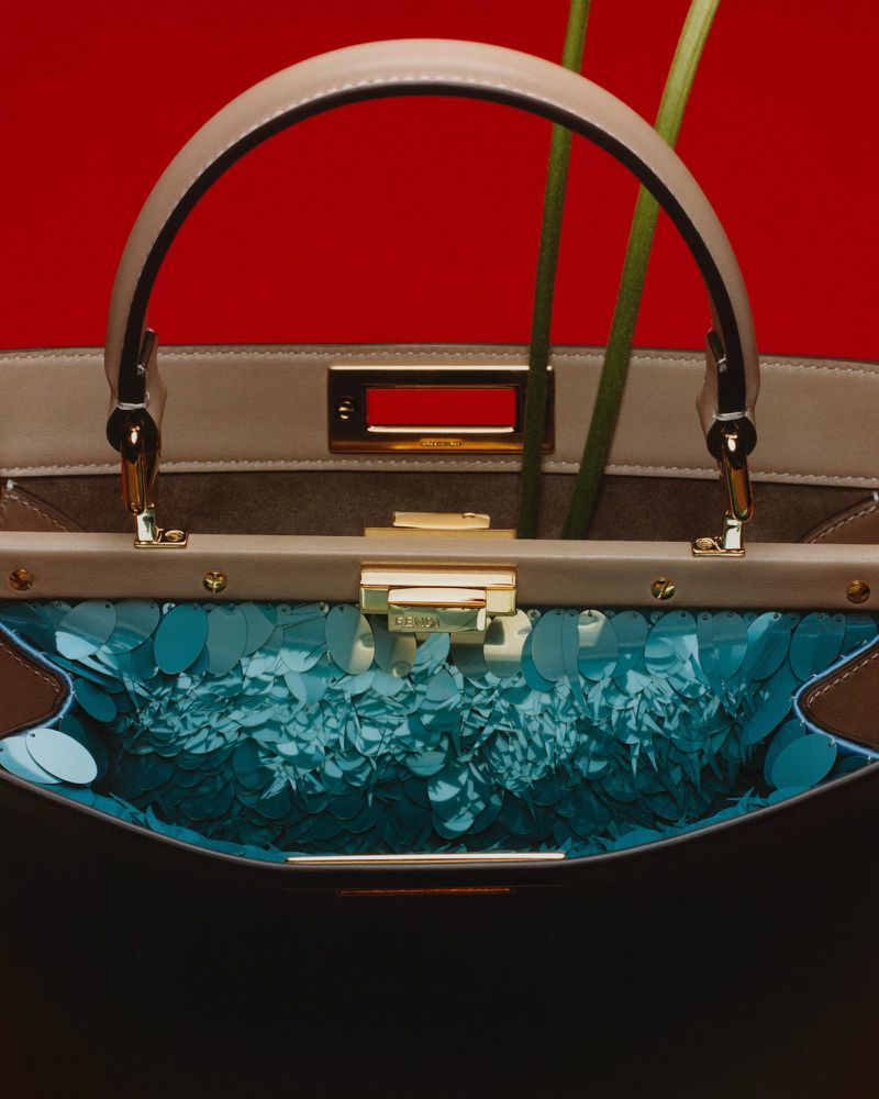 Open beige leather handbag with teal sequin interior and green stems against a solid red background