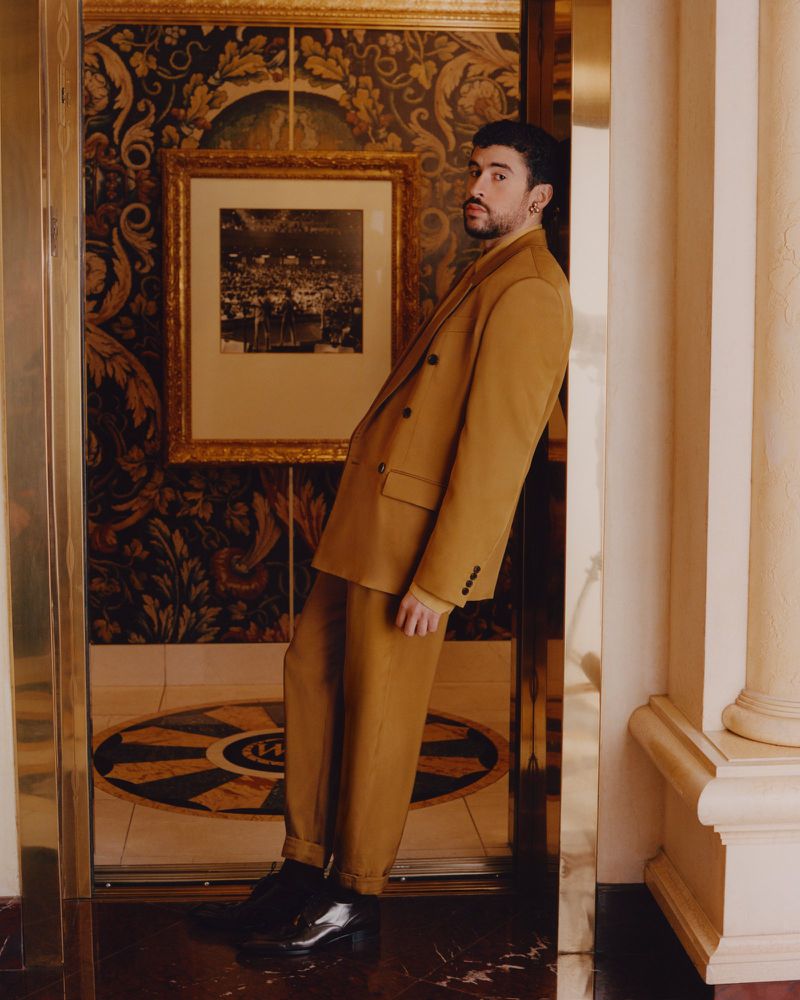 Bad Bunny leaning against a doorway in a mustard suit for American Vogue King Of The Road project
