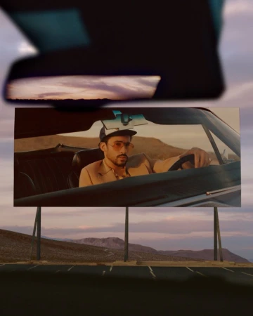 Bad Bunny driving a car depicted on an outdoor billboard under a sunset sky