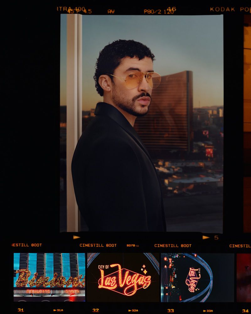 Bad Bunny wearing tinted sunglasses and a dark jacket against a skyline view framed by film strips with neon signs