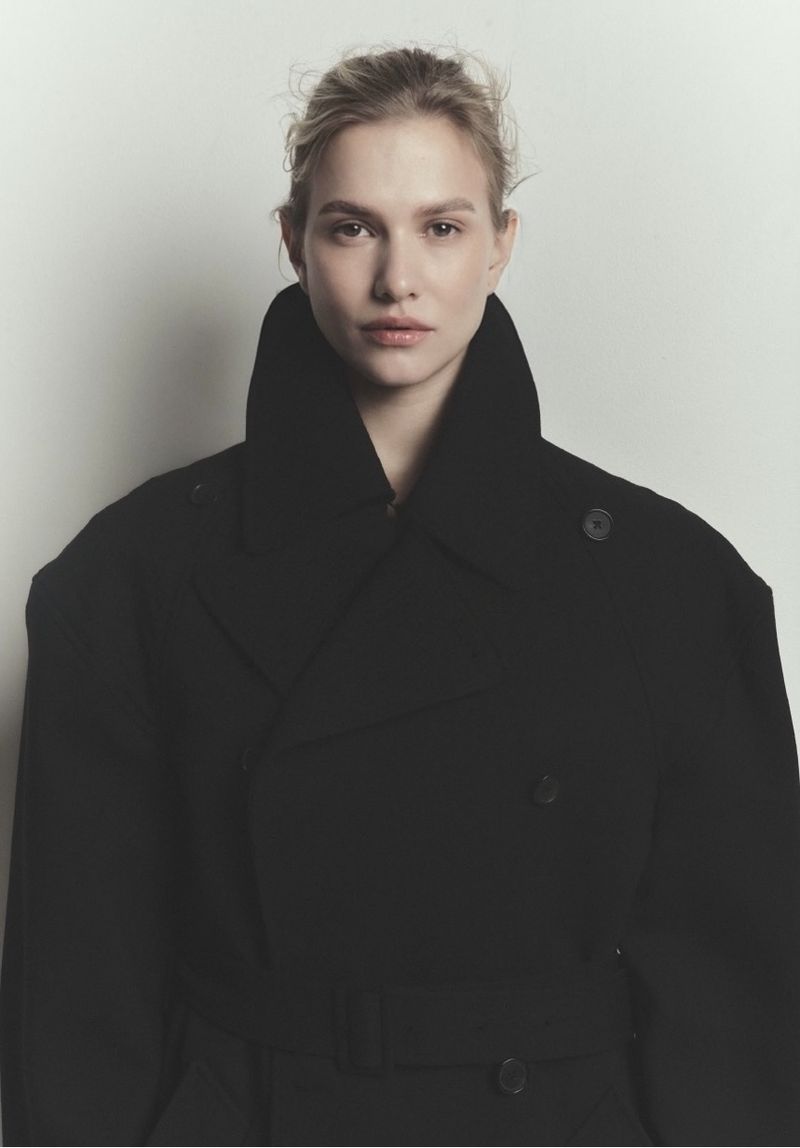 Model wearing a black coat with a high collar against a neutral white background for Vanguard Magazine