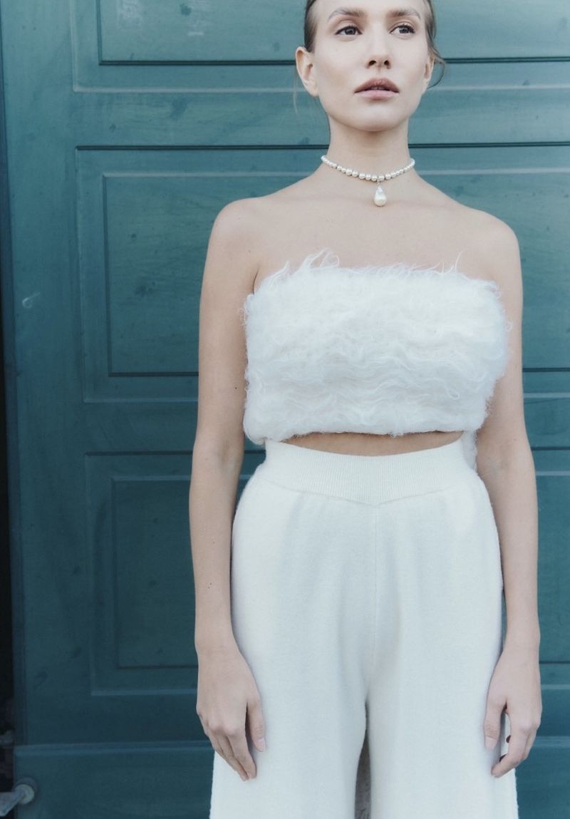 Model wearing a white furry strapless top and white trousers in front of a green wooden door for Vanguard Magazine