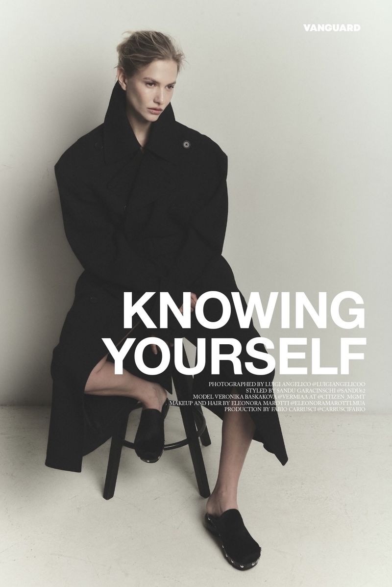 Model Veronika Baskakova seated on a stool wearing a long black coat for Vanguard Magazine