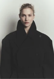 Model wearing a black coat with a high collar against a neutral white background for Vanguard Magazine