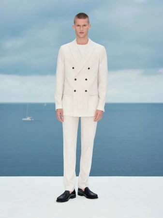 Model standing outdoors wearing a cream double-breasted suit against an ocean background for Marks and Spencer
