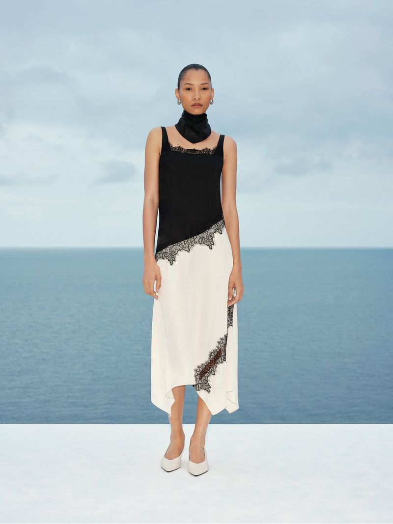 Model standing outdoors wearing a black and white dress against a calm ocean backdrop for Marks & Spencer