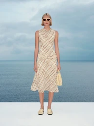 Model wearing patterned dress and sunglasses holding handbag against ocean backdrop