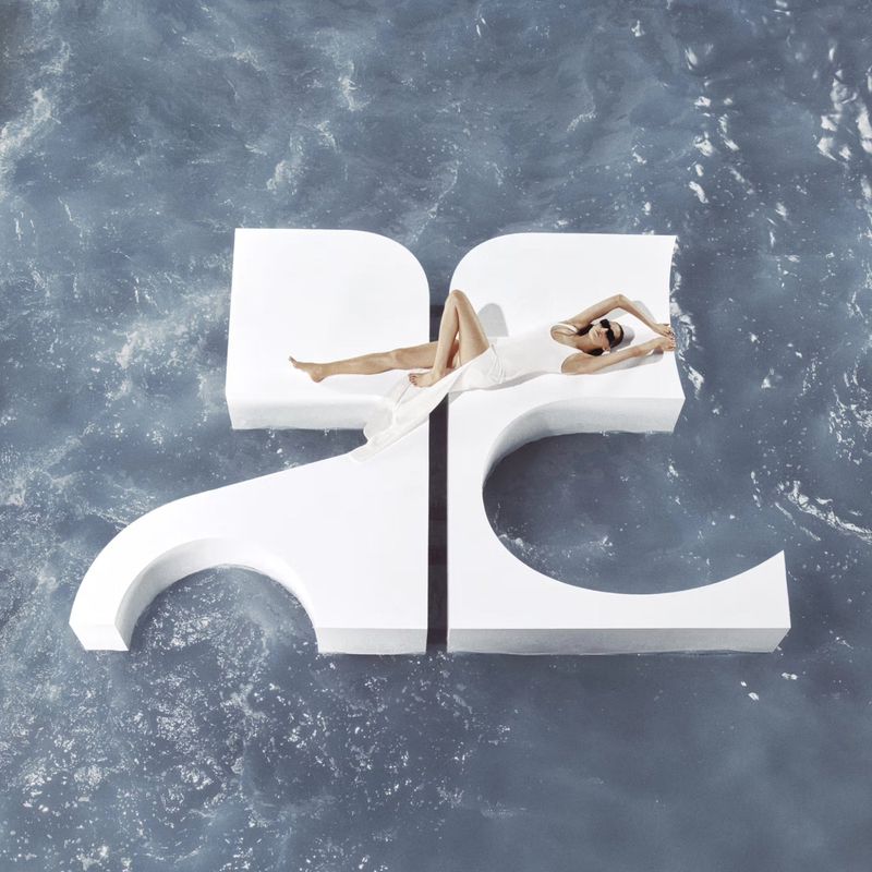 Model lying on a large white Courreges logo structure floating in rippling water