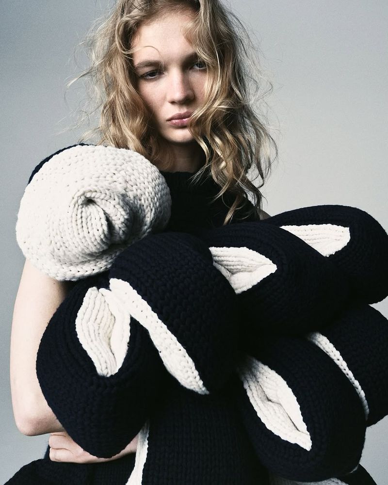 Fashion shot featuring a blonde adult female with light skin, wearing a black top and a black and white knitwear piece.