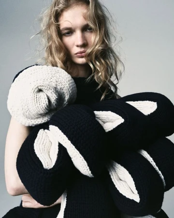 Model Caitlin Soetendal holding sculptural black and white chunky knitwear loops against a neutral studio background.