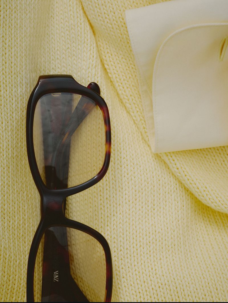 Tortoiseshell eyeglasses resting on a textured yellow knit sweater next to a white cuff