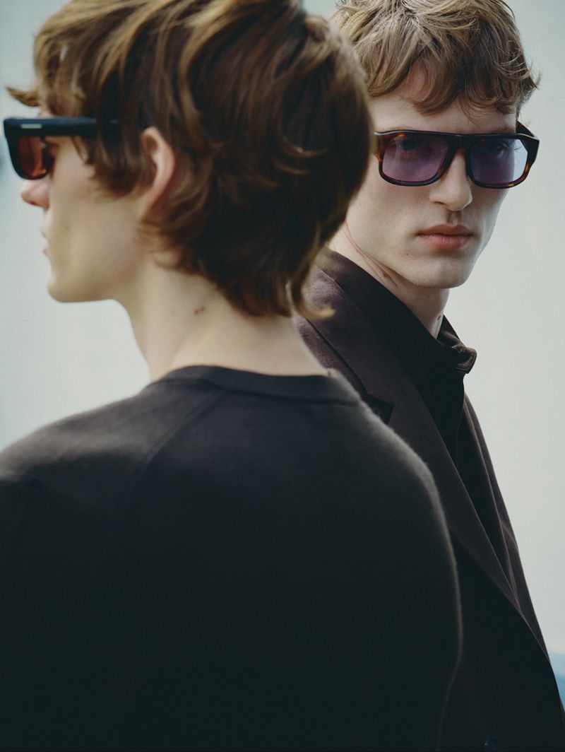 Two male models wearing dark sunglasses and dark clothing against a plain light background for Zara Man.