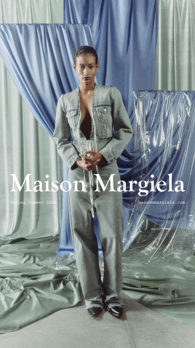 Fashion editorial featuring a woman in a denim jacket and jeans, posing against a draped blue backdrop with a modern, minimalist aesthetic.