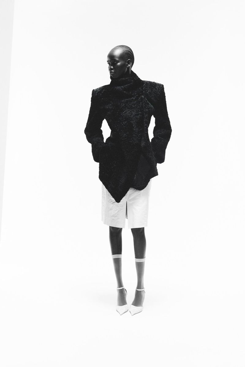 Black model standing against a white backdrop wearing a textured dark jacket and white shorts.