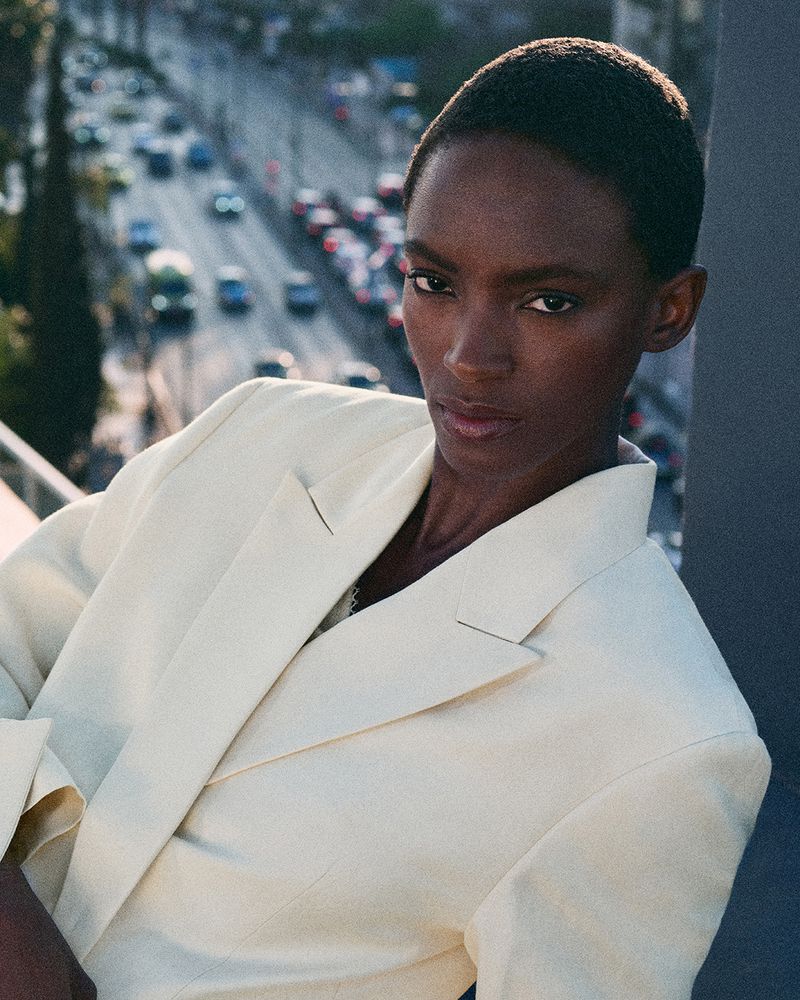 Model in light cream blazer posing against a blurred urban street backdrop for COS campaign