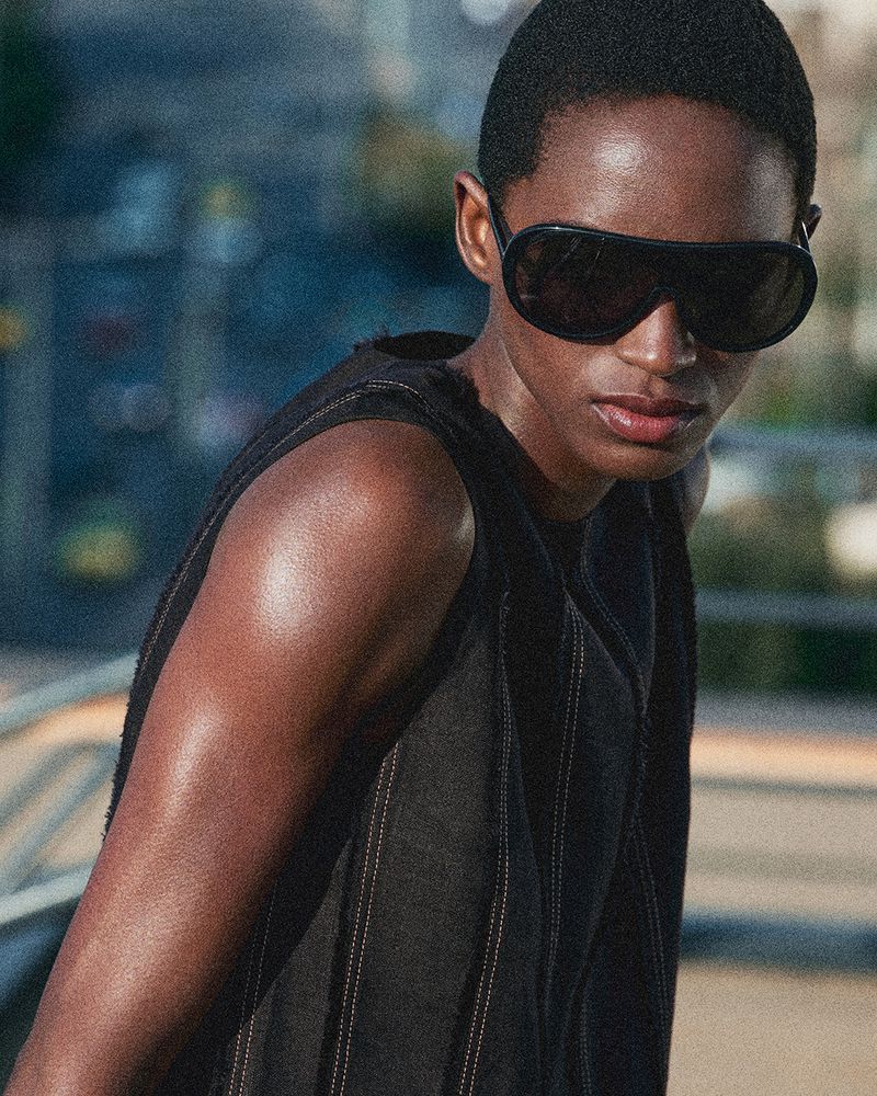 Model with dark sunglasses wearing a black sleeveless top against an urban outdoor background for COS summer in the city project