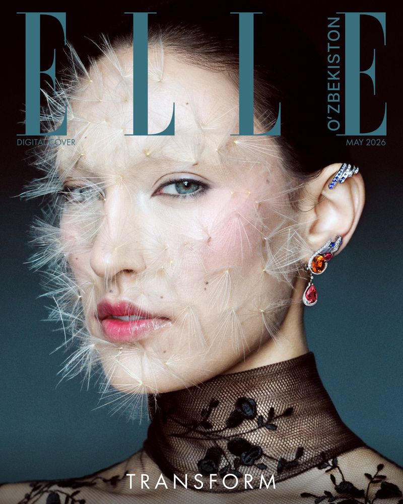 Close-up portrait of a woman with delicate dandelion seeds covering her face and a black sheer lace top against a dark background