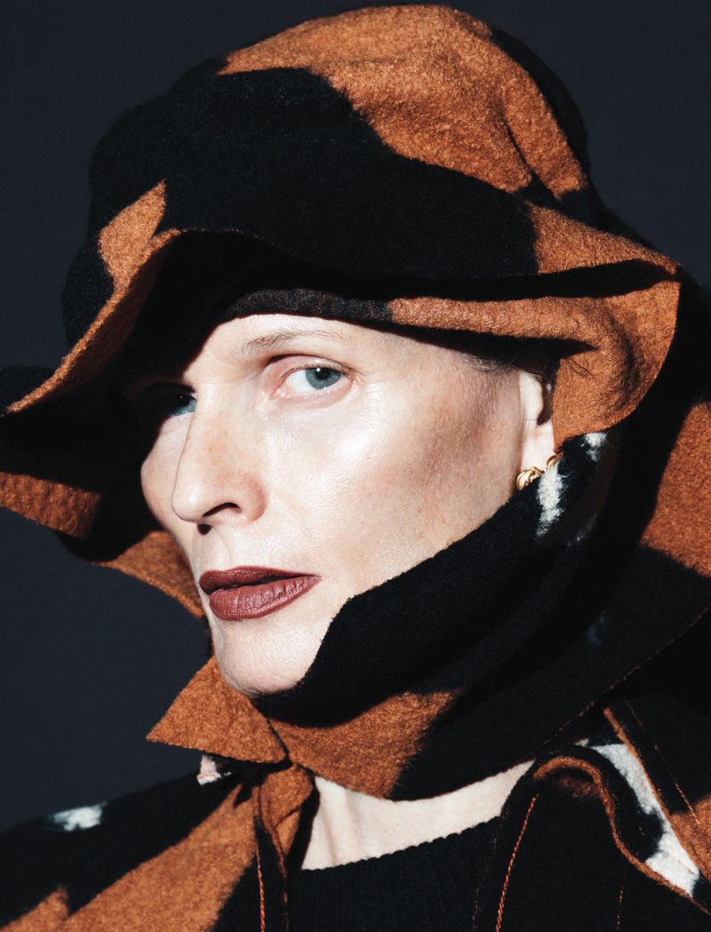 Woman with fair skin and blue eyes poses with a patterned hat and cowl neck piece in a beauty and fashion close-up studio shot.