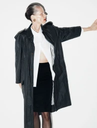 Model in a black trench coat over a white shirt and black skirt against a plain white background for Reserved Magazine