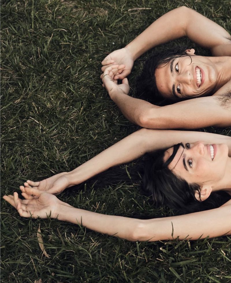 Two models lying on green grass with arms raised above their heads for Calvin Klein denim campaign photographed by Bryan Liston.
