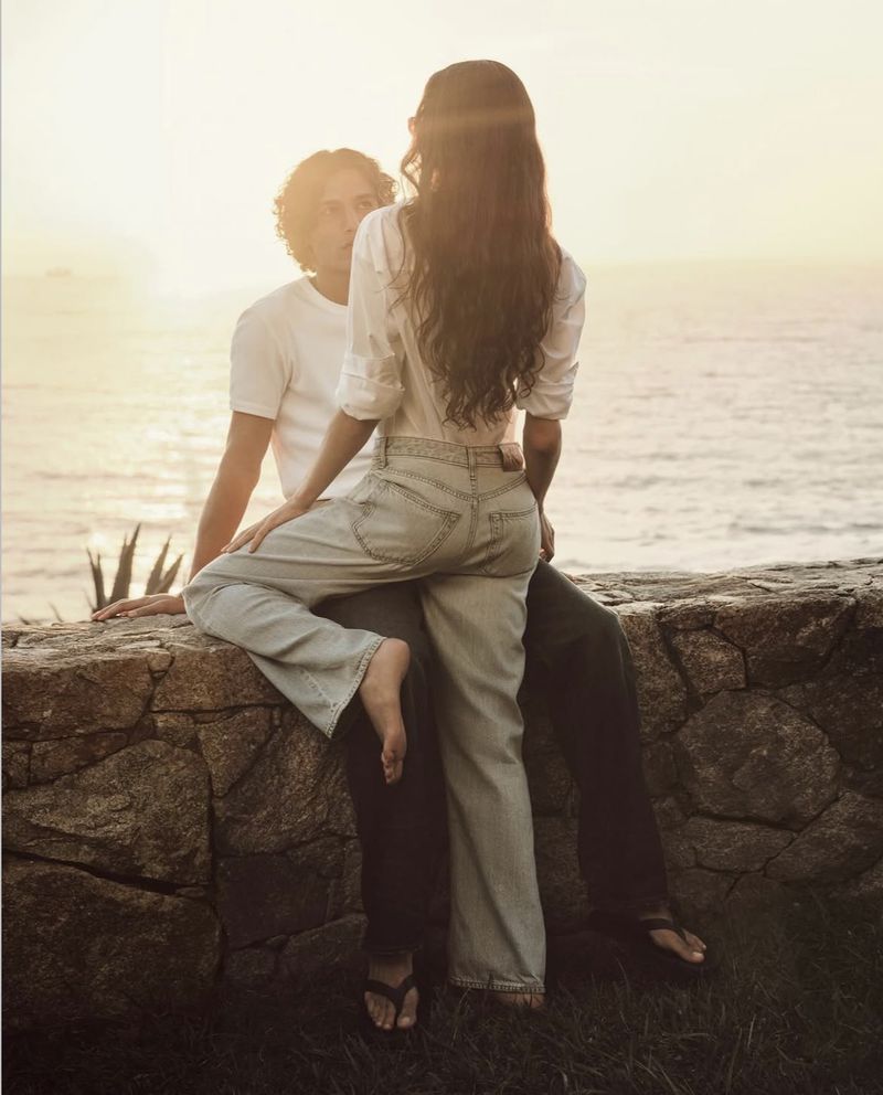Man and woman sitting together on a stone wall overlooking the ocean at sunset for Calvin Klein