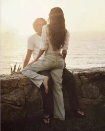 Man and woman sitting together on a stone wall overlooking the ocean at sunset for Calvin Klein