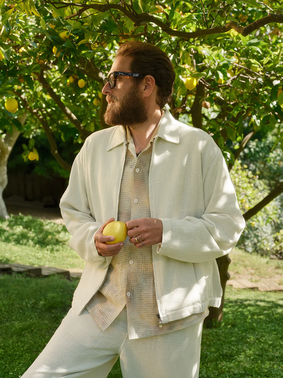 Jonah Hill wearing a light jacket and patterned shirt holding a lemon under a tree for Kith