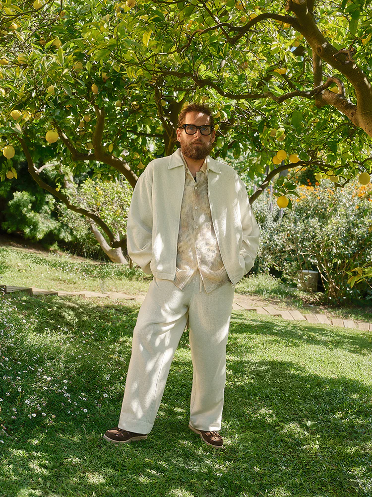 Jonah Hill standing outdoors under a lemon tree wearing a light-coloured jacket and trousers for Kith Life Lessons