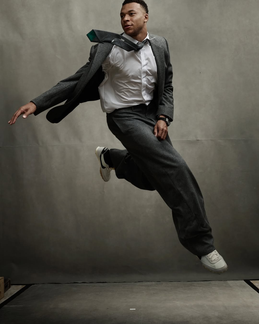 Kylian Mbappe mid-air jumping wearing a grey suit and tie against a grey backdrop for Vanity Fair U.S.