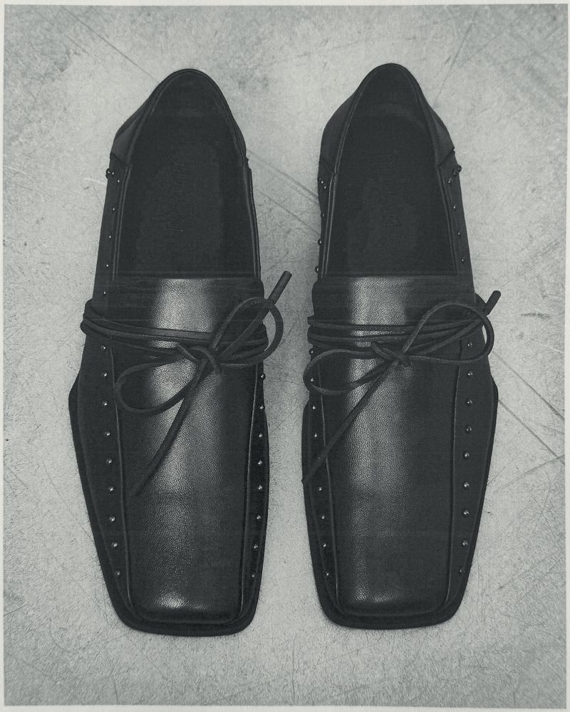 Top-down view of black leather dress shoes with stud details and tied laces placed on a concrete floor.