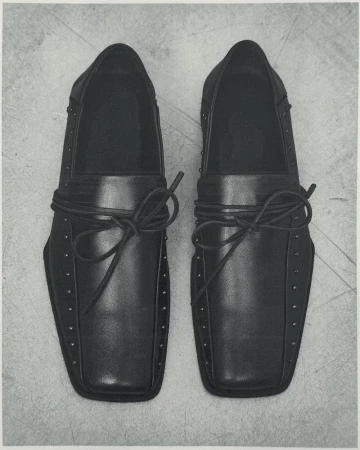 Top-down view of black leather dress shoes with stud details and tied laces placed on a concrete floor.