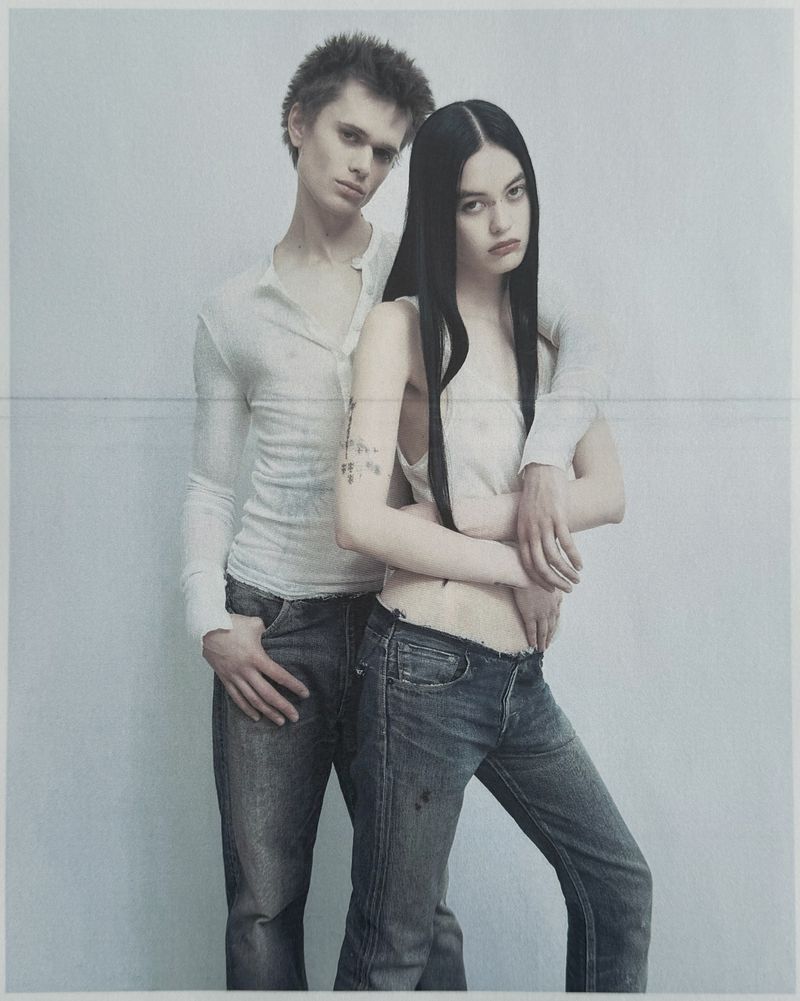 Portrait of a man and a woman posing together against a plain grey background for Unvain Studios SS26.