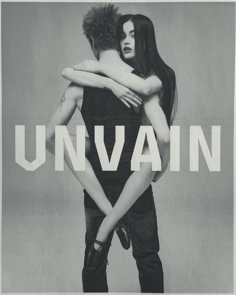 Monochrome fashion campaign image featuring a woman hugging a man from behind against a plain studio background with bold white typography.